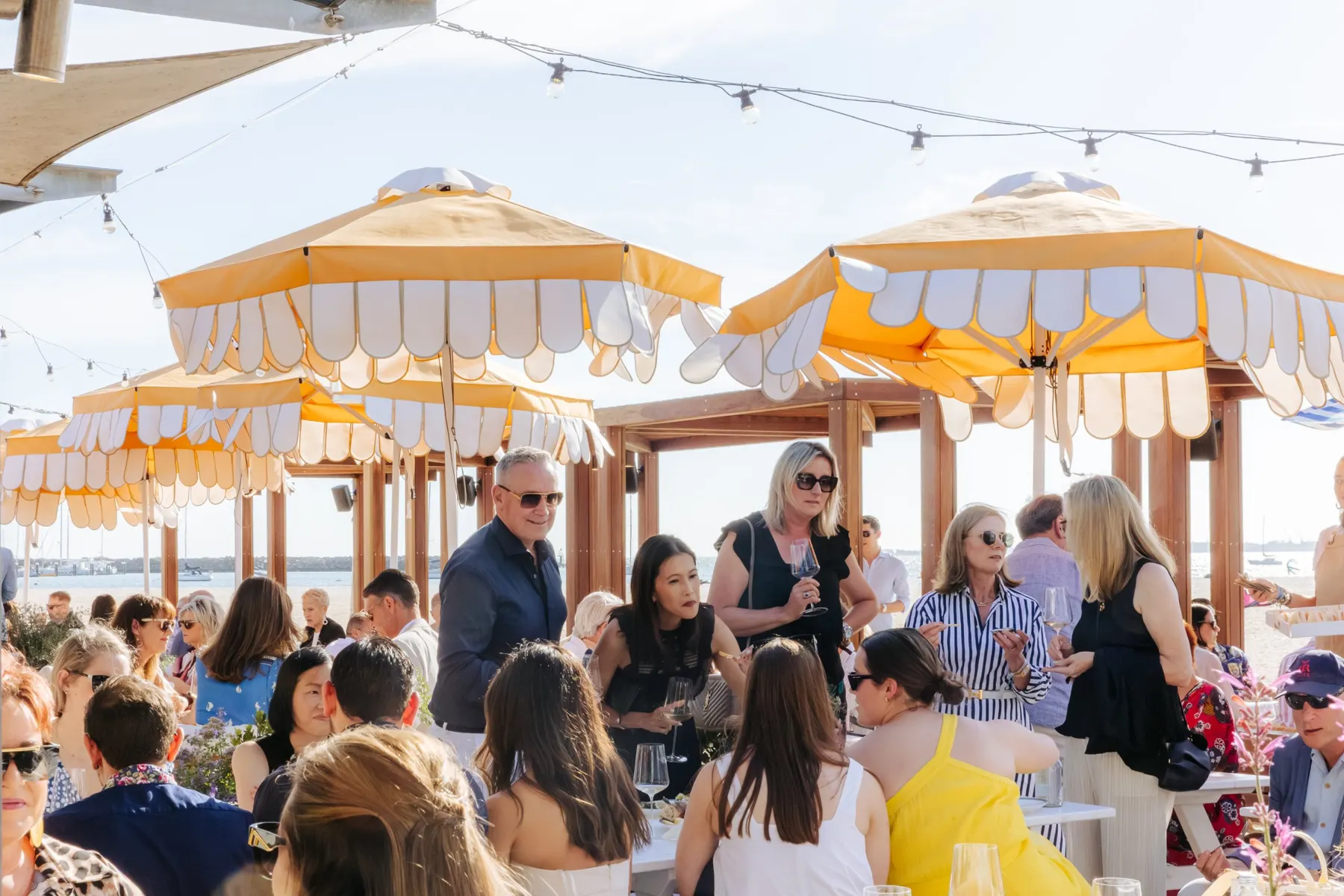 Members talking over glasses of wine beneath yellow scalloped umbrellas