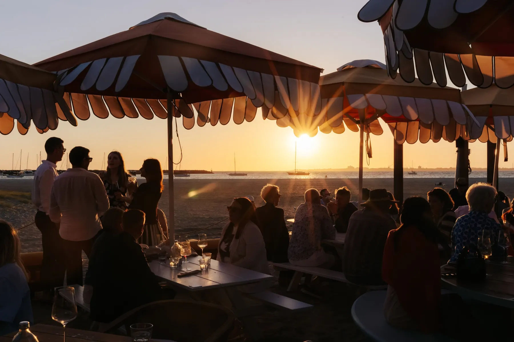 Members at long tables under scalloped umbrellas as the sun sets over the bay